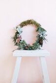 Wreath of twigs, moss and succulents leaning against wall on white wooden stool