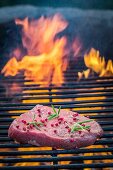A fresh steak seasoned with pepper and rosemary on a grill rack with fire