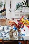 Ethnic sculpture and glass vase holding twigs of colourful leaves on coffee table