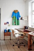 Rustikaler Holztisch und Retro Bürostuhl mit Schaffell neben Nähkasten mit Garnspulen, Kleid als Wanddekoration
