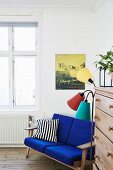 Sofabank mit blauen Polstern neben Retro Stehlampe und Kommode