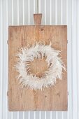 Wreath of feathers on old chopping board hung on radiator