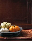 An arrangement of three decorative pumpkins in a grey metal dish