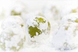 Balls of raw biscuit dough with matcha and white chocolate rolled in icing sugar