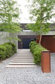 Stepping stones amongst gravel leading to concrete wall and modern house
