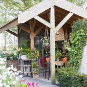 Blick in halboffenes Gartenhaus mit verschiedenen Topfpflanzen und Blumenampeln