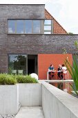 Modern brick extension with people sitting on concrete terrace and pool
