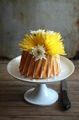 A yellow cake with flowers on a cake stand