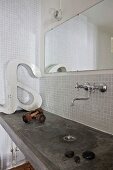 Beton-Waschtisch, nostalgische Wandarmatur und Wandspiegel in Bad mit weißer Mosaikfliesenwand
