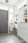 White chest of drawers, coat pegs and grey front door in bright hallway
