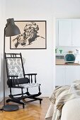 Black wooden rocking chair next to standard lamp and below black-framed drawing on wall