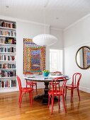 Essplatz mit rundem Tisch und roten Bugholzstühlen in Altbauwohnung mit Bücherregal und buntem Gemälde