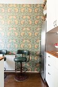Dark green retro bar stools against floral wallpaper in kitchen