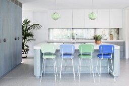 Schlichte Küche in Weiß-Graublau mit blauen und grünen Barhockern an Kücheninsel