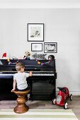 Junge sitzt auf gedrechseltem Holzhocker am Klavier