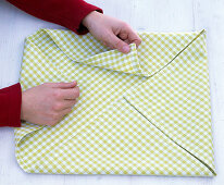 Folding a green and white checked cloth napkin (1/5)