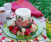 Wreath of blossoms of Rosa (roses, light pink, pink and red) around candle