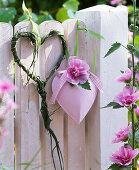 Alcea 'Parkrondell' (Stockrose) an Herz, Herz aus Gräsern gewunden am Zaun