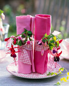 Fuchsia (fuchsias) with ribbons on rolled up, pink napkins