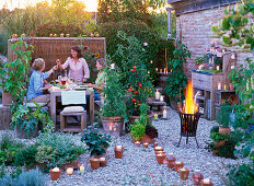 LOHAS - Serie: Abendliche Terrasse mit Kerzen und Feuerkorb, Lycopersicon (Tomate), Lathyrus odoratus (Duftwicken), Phaseolus coccineus (Feuerbohnen), Cucurbita (Zucchini), Topfturm und Kasten mit Kräutern, Freunde am Tisch