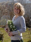 Junge Frau bringt Holzkasten mit Galanthus (Schneeglöckchen)