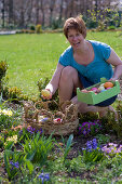 Frau füllt Osternest im Blumenbeet mit bunten Ostereiern