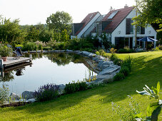 Swimming pond with wooden deck, bordered with granite stones and perennials