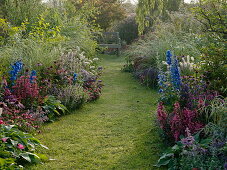 Lawn path between beds with perennials, summer flowers and grasses