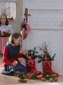 Girl next to red Father Christmas boots filled with Abies (fir), apples
