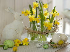 Narcissus 'Tete a Tete' (Narzissen), kleine Flaschen als Vasen im Strohkranz