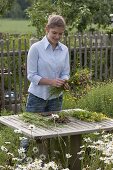 Junge Frau bindet Strauß aus Wiesenblumen 1/2