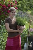 Junge Frau hält Topf mit Lavendel (Lavandula) im Arm