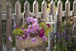 Tasche mit Sommerblumen als Willkommensgruß an Gartentor gehängt