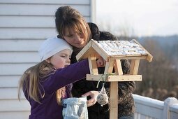 Mutter und Tochter befüllen ein Vogelfutterhaus