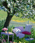 Green wooden bench and pink side table under flowering Malus