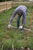 Garden planning, man measuring path width and recording it with color powder