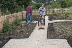 Men laying off gravel, solidify with vibratory plate