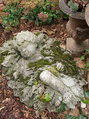Moosbewachsene Figur aus Zement: schlafendes Kind im Blätterbett
