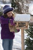 Girl filling bird house with sunflower seeds