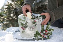 Homemade ice lantern with frozen leaves and berries of holly