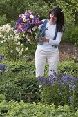 Frau im Garten mit Strauß aus Aquilegia (Akelei), Syringa (Flieder)