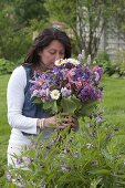 Frau im Garten schnuppert an Strauß aus Aquilegia (Akelei), Syringa (Flieder)