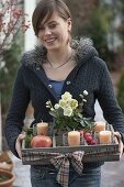 Woman brings wooden box as Advent wreath with 4 candles, pot with Helleborus niger