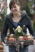 Frau bringt Holz-Kiste als Adventskranz mit 4 Kerzen, Topf mit Helleborus niger