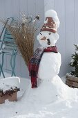 Snowman with clay pot as hat, scarf, cabbage stalk as pipe, carrot as nose