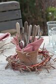 Cutlery with red-white checked napkin in terracotta vase, wreath of Corylus