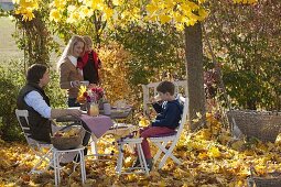 Familie am Tisch im goldenen Herbstlaub unter Ahornbaum
