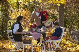 Family at table in golden autumn leaves under maple tree