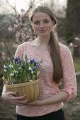 Woman carrying woodchip basket with Galanthus nivalis and Iris