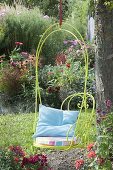 Hanging armchair on the tree, flower beds with summer flowers and perennials